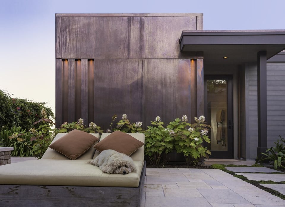 Custom patio with dog resting on outdoor daybed beside copper facade in Tiburon home by S.A. Baxter, Inc.